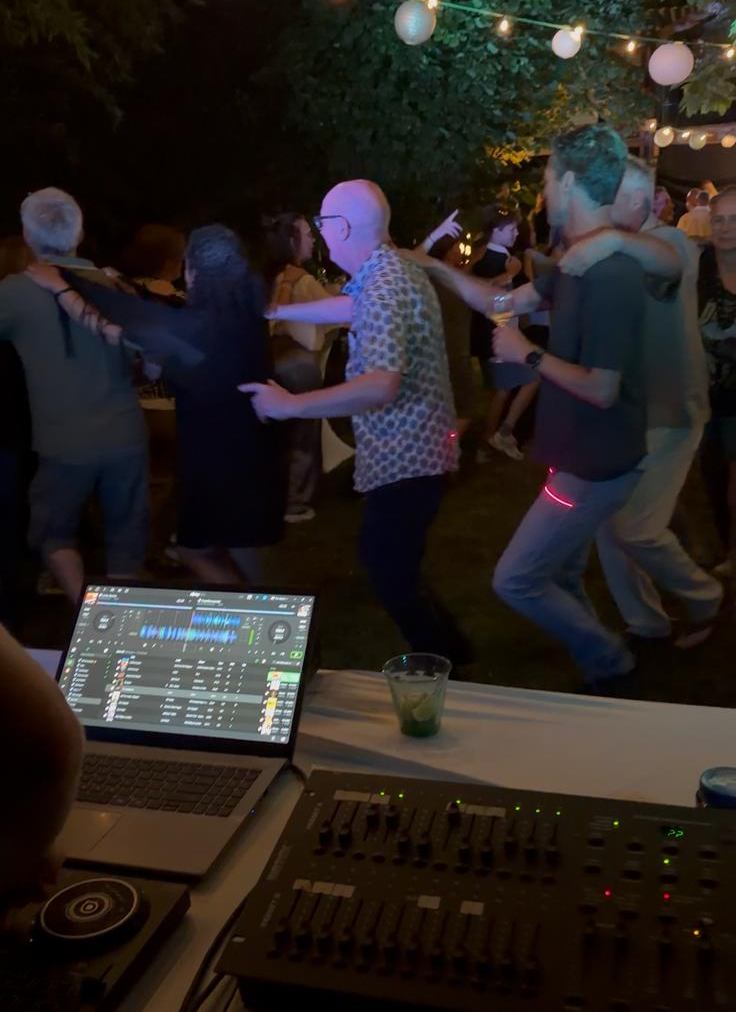 Gasten dansen in een tuin onder de lampionnen, met de lichttafel op de voorgrond