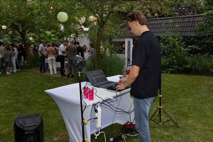 DJ-opstelling in een tuin met lampionnen en gasten op de achtergrond